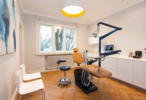 Moderner Zahnarztpraxisraum mit Behandlungsstuhl, Geräten und hellem Parkettboden.